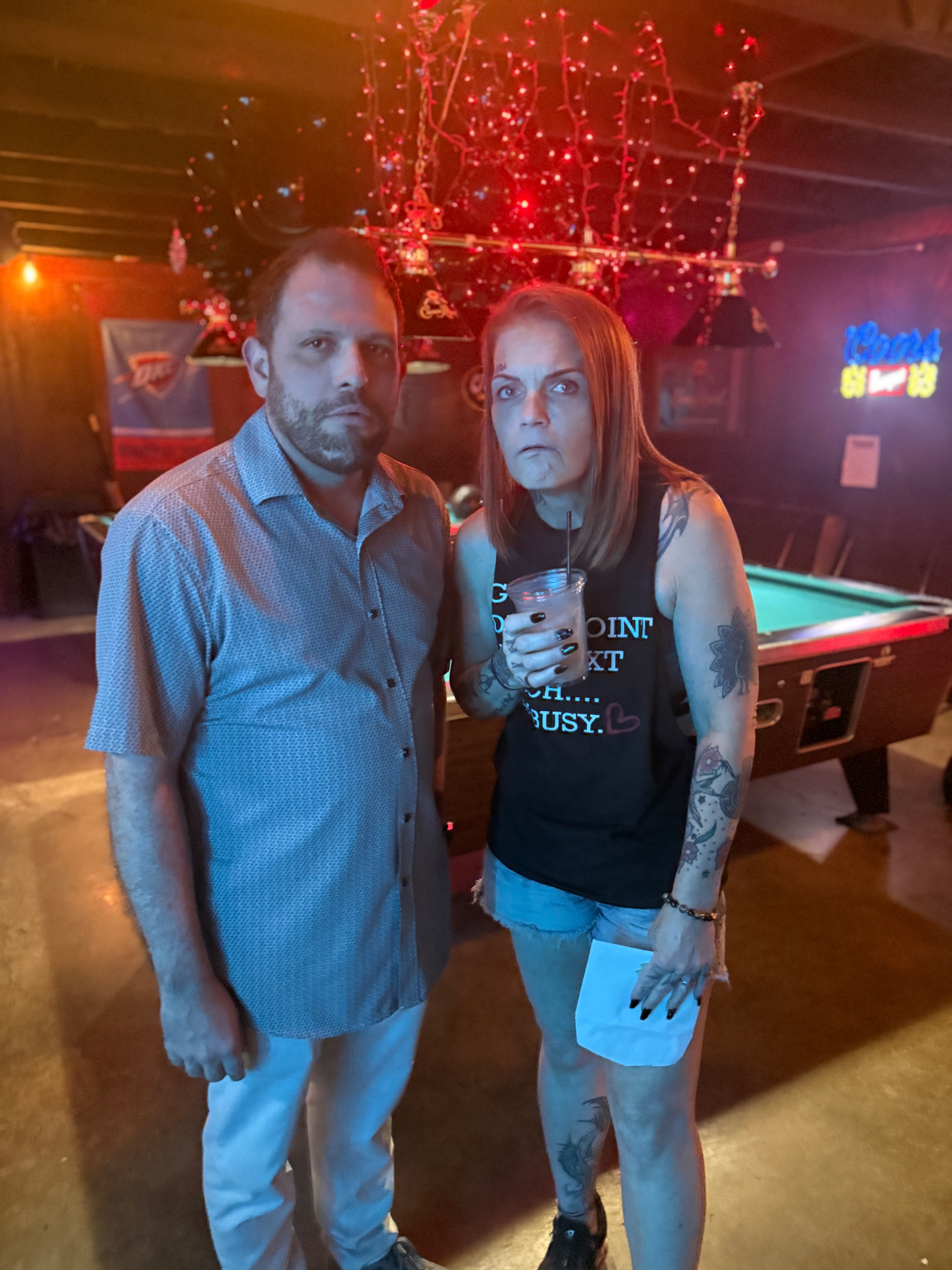 Two regulars posing by the pool table under the string lights